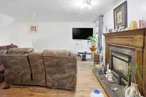 Living room featuring light wood-type flooring, a textured ceiling, and a tile fireplace