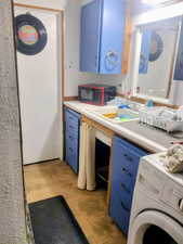 Kitchen featuring blue cabinetry, washer / clothes dryer, light countertops, black microwave, and unfinished concrete floors