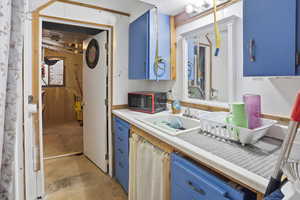 Kitchen with blue cabinetry, light countertops, unfinished concrete flooring, and black microwave