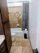 Bathroom featuring shower / bathtub combination with curtain, vanity, and stone tile flooring