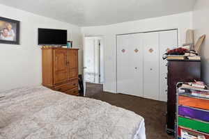 Bedroom with a closet, a textured ceiling, and dark carpet
