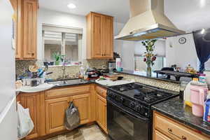 Kitchen with black gas range, island range hood, dark stone counters, and brown cabinetry