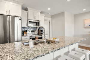 Kitchen featuring stainless steel appliances, white cabinets, light stone countertops, a textured ceiling, and recessed lighting