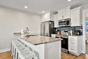 Kitchen featuring a peninsula, appliances with stainless steel finishes, a kitchen bar, light wood-style floors, and white cabinets