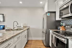 Kitchen with appliances with stainless steel finishes, white cabinetry, light stone counters, light wood-type flooring, and recessed lighting