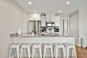 Kitchen with a peninsula, a breakfast bar, appliances with stainless steel finishes, white cabinets, and recessed lighting