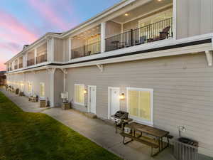 Back of house at dusk featuring board and batten siding, a balcony, a yard, and a patio