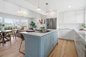 Kitchen with blue cabinets, white cabinetry, stainless steel fridge with ice dispenser, light stone counters, and a center island
