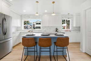 Kitchen featuring decorative light fixtures, stainless steel fridge, a kitchen island, white cabinetry, and recessed lighting