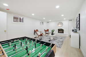 Game room with a fireplace with raised hearth, light wood-type flooring, and recessed lighting