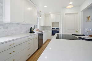 Kitchen featuring white cabinets, appliances with stainless steel finishes, light wood-type flooring, hanging light fixtures, and decorative backsplash