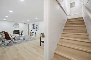 Stairs with wood finished floors, recessed lighting, and a fireplace with raised hearth
