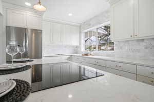 Kitchen featuring stainless steel refrigerator with ice dispenser, light stone counters, black electric cooktop, white cabinets, and recessed lighting