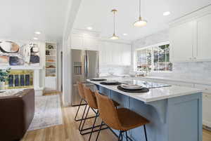 Kitchen featuring stainless steel fridge with ice dispenser, a breakfast bar area, white cabinetry, light stone counters, and recessed lighting