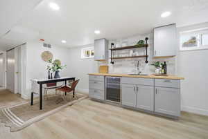 Indoor wet bar featuring open shelves, butcher block counters, beverage cooler, gray cabinetry, and recessed lighting
