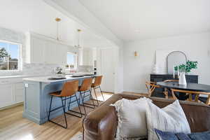 Kitchen featuring open floor plan, a breakfast bar, white cabinets, and decorative light fixtures