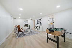 Recreation room featuring a fireplace with raised hearth, light wood-type flooring, recessed lighting, and wine cooler