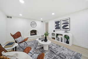 Living area featuring a fireplace with raised hearth, light wood-style floors, and recessed lighting