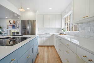 Kitchen with stainless steel fridge with ice dispenser, blue cabinets, black electric stovetop, light stone countertops, and white cabinetry