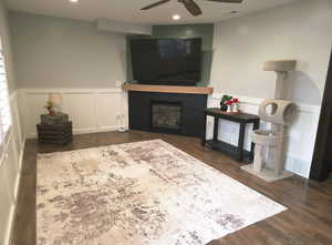 Living area with wainscoting, a decorative wall, a large fireplace, dark wood-type flooring, and recessed lighting