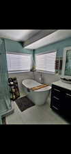 Full bath with a freestanding bath, a shower stall, light tile patterned flooring, tile walls, and vanity