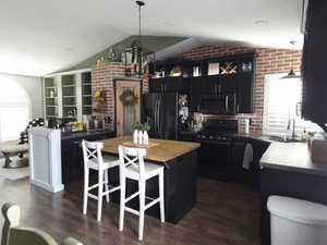Kitchen with dark cabinets, butcher block countertops, decorative light fixtures, black appliances, and vaulted ceiling