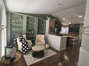 Living area with vaulted ceiling, dark wood-style flooring, brick wall, recessed lighting, and built in features