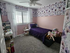 Carpeted bedroom featuring wallpapered walls, ceiling fan, and a wainscoted wall