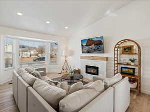 Living room featuring lofted ceiling, a tiled fireplace, light wood-style flooring, and recessed lighting