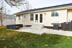 Rear view of property featuring a patio area, roof mounted solar panels, a fenced backyard, french doors, and entry steps