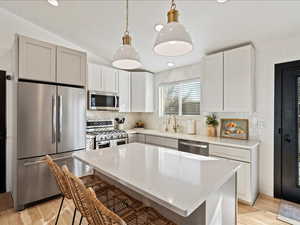 Kitchen featuring stainless steel appliances, lofted ceiling, decorative light fixtures, a breakfast bar, and light stone counters