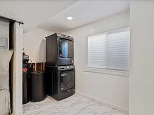 Washroom with light marble finish floors, stacked washing machine and dryer, and recessed lighting