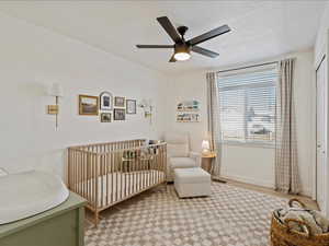 Bedroom with a nursery area, wood finished floors, a ceiling fan, and a textured ceiling