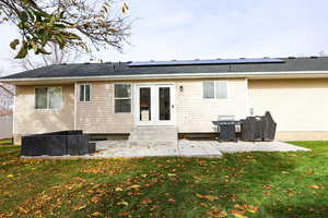 Back of house with a patio area, roof mounted solar panels, a lawn, and french doors