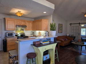 Kitchen featuring a kitchen bar, a textured ceiling, electric stove, a barn door, and ceiling fan