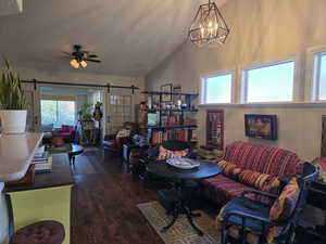 Living area featuring plenty of natural light, dark wood-style floors, a barn door, ceiling fan, and high vaulted ceiling