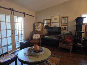 Living area featuring a barn door, dark wood-style flooring, a textured ceiling, and vaulted ceiling