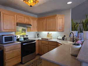 Kitchen with electric range, a textured ceiling, under cabinet range hood, tile patterned flooring, and a peninsula