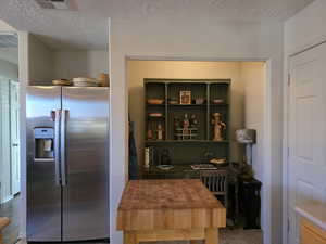 Kitchen featuring stainless steel refrigerator with ice dispenser and a textured ceiling