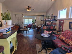 Living room with lofted ceiling, a barn door, dark wood-type flooring, a ceiling fan, and a textured ceiling