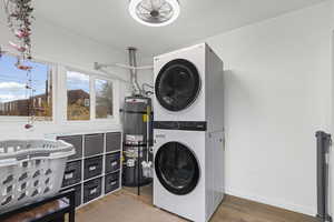 Washroom featuring stacked washing machine and dryer, secured water heater, and light wood finished floors