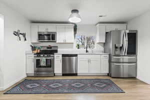 Kitchen featuring white cabinets, appliances with stainless steel finishes, and light wood finished floors