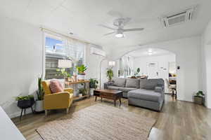 Living room featuring a ceiling fan, arched walkways, light wood finished floors, and a wall unit AC
