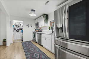 Kitchen featuring stainless steel appliances, white cabinets, light countertops, and light wood-type flooring