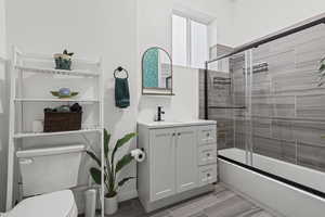 Bathroom with vanity, bath / shower combo with glass door, and wood finish floors