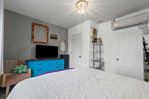 Bedroom with a textured ceiling, an AC wall unit, and a closet