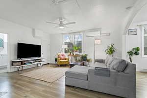 Living room featuring a ceiling fan, light wood-type flooring, and a wall mounted air conditioner