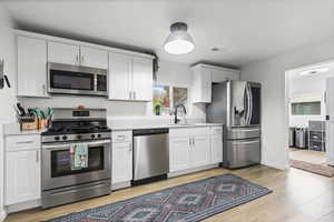 Kitchen with stainless steel appliances, white cabinets, and light wood-type flooring