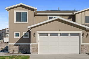 View of front of property featuring stone siding, concrete driveway, stucco siding, and a shingled roof
