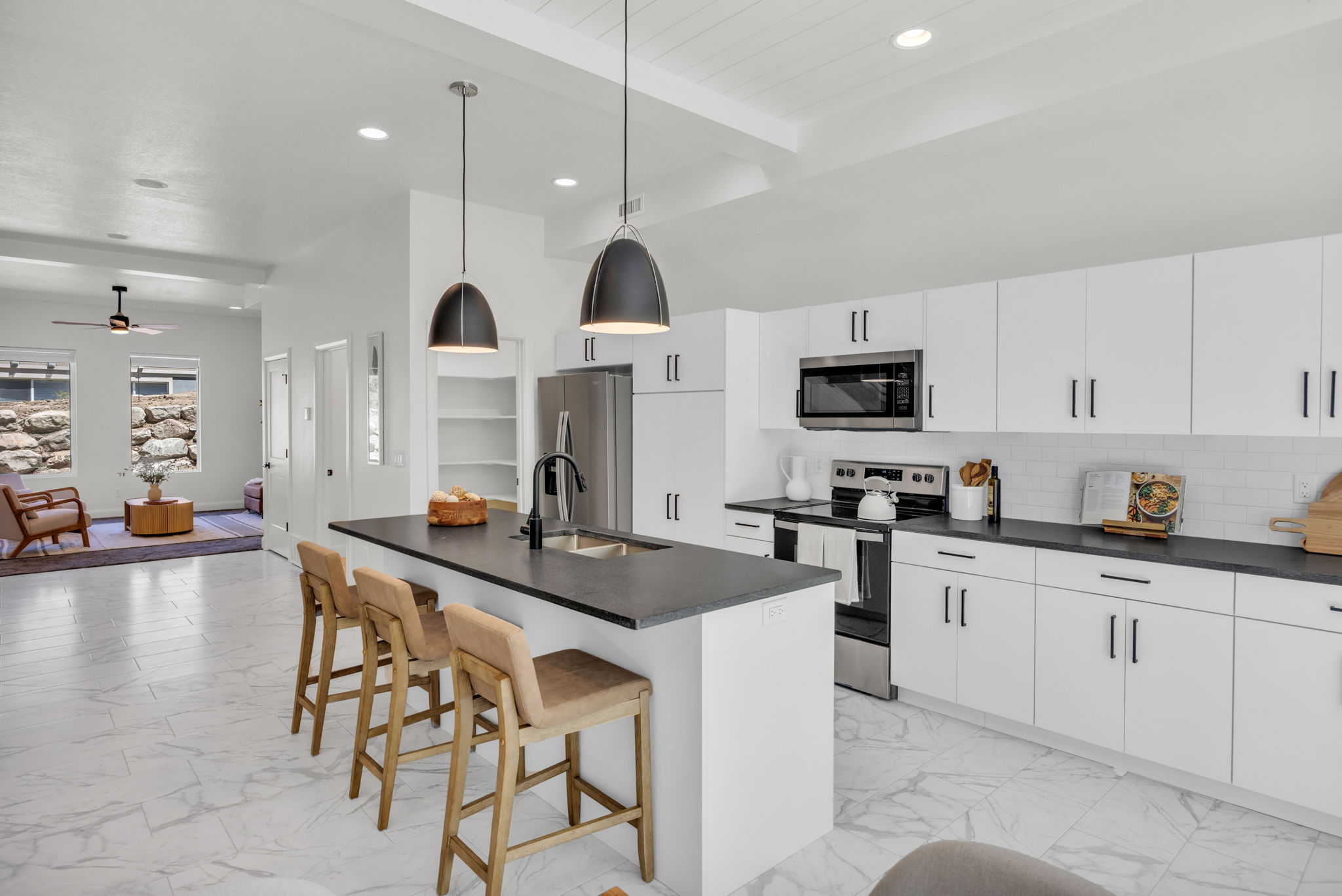 Kitchen featuring light marble finish floors, appliances with stainless steel finishes, dark countertops, a kitchen island with sink, and beamed ceiling
